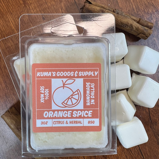 Kuma's Goods & Supply orange spice wax melt packaging on a wooden surface with cinnamon sticks.